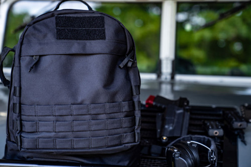 Black Pecos Backpack beside handgun and headphones.