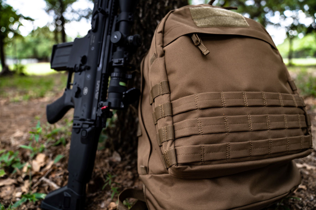 Coyote Brown Pecos Backpack next to firearm standing up against tree.