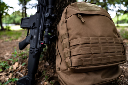 Coyote Brown Pecos Backpack next to firearm standing up against tree.