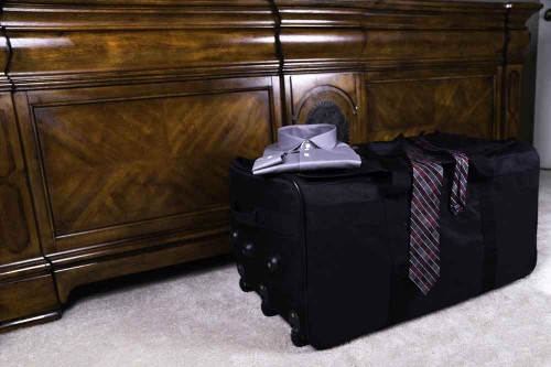 Black Buffalo Duffel in bedroom on side showing foot locker profile & rigid structure with clothes on top of it.