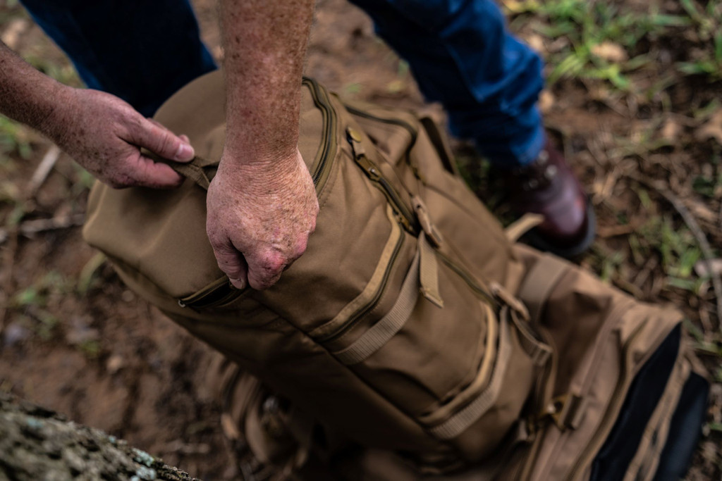 Unzipping the top lid of the GTFO Top Load Duffel Backpack in coyote brown.