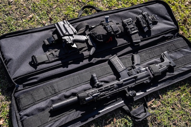 Black Single Rifle Case opened on ground with firearms inside.