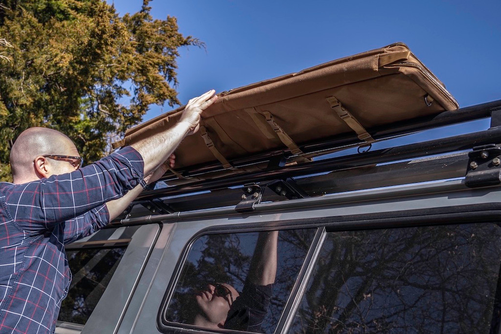 Coyote brown Single Rifle Case being attached to racks on top of grey sports utility vehicle.