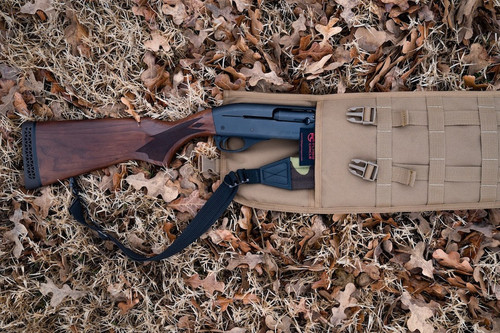 The top end of a Coyote Brown Shotgun Scabbard on the ground with brown leaves. There is a brown and black rifle inside the scabbard and the stock is seen outside of the top.