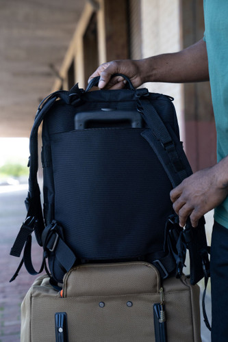 Back of black Midland Backpack sitting on top of coyote brown Mini Buffalo Rolling Duffel showing the top and bottom zippers of the back pocket of the backpack unzipped and slipped over the rolling luggage handle for easy towing.